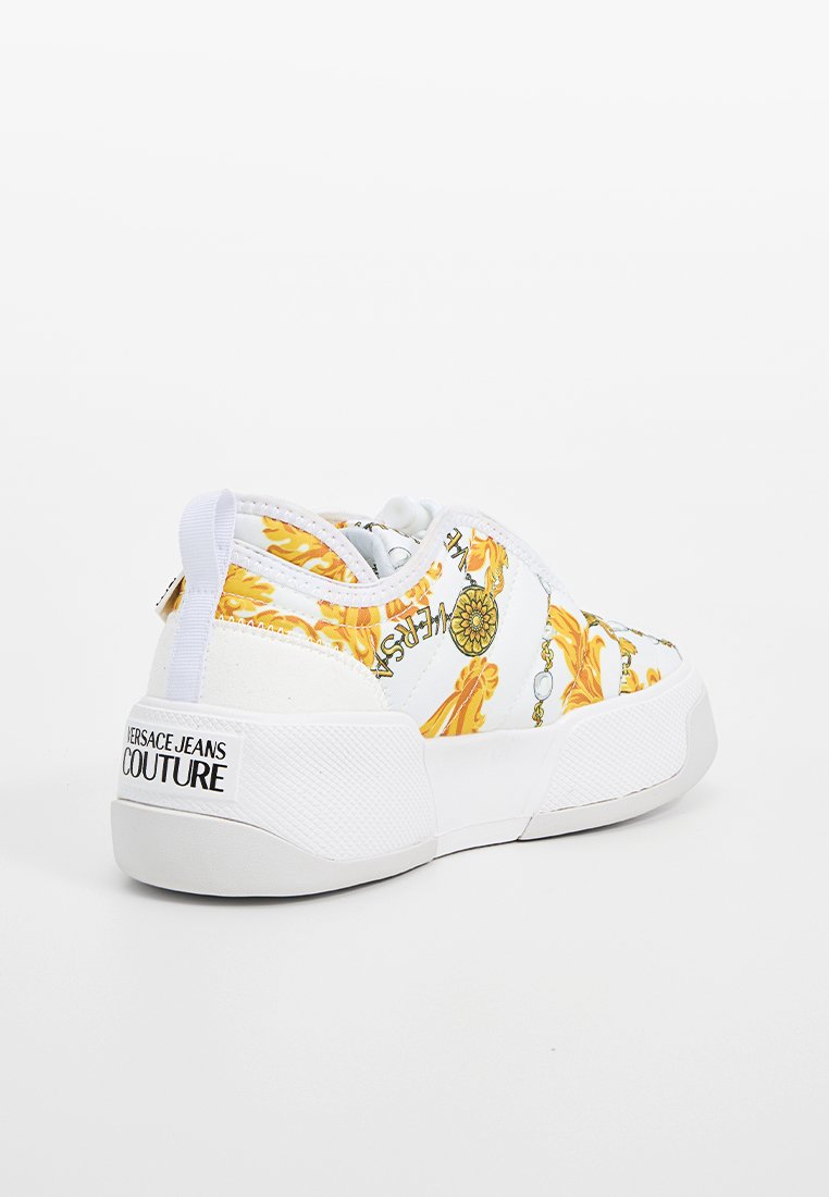 Weiße Versace Jeans Couture Sneaker mit gelbem barockem Muster, dicker Sohle und Marken-Logo an der Ferse vor einem schlichten weißen Hintergrund.