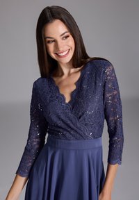 Abito blu navy con corpetto in pizzo, scollatura a onda e maniche a tre quarti, abbinato a una gonna fluente e uniforme.