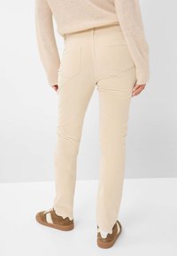 Beige Baumwollmischungshosen mit Gesäßtaschen, geradem Schnitt und dezenten Steppnähten, kombiniert mit braunen Wildledersneakers.