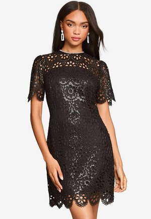 Black lace dress featuring floral embroidery, short sleeves, scalloped hem, and a fitted silhouette. Details include sequin accents.