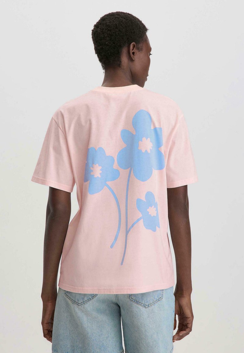 Lichtroze katoenen T-shirt met een blauwe bloemenprint op de achterkant. Korte mouwen en een ronde hals, met een relaxte pasvorm.