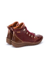 Bottes de cheville en cuir marron et bordeaux avec des œillets en or, un col en tricot texturé et une épaisse semelle en caoutchouc. Détails de couture renforcés visibles.