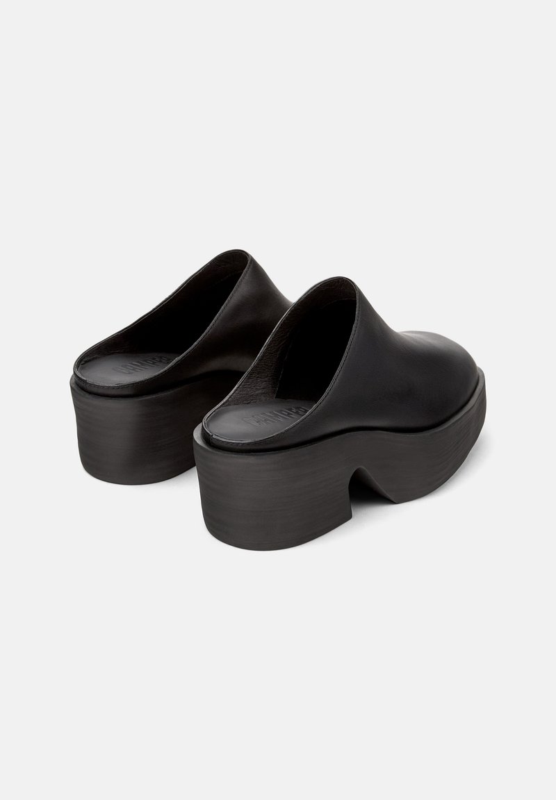 Zuecos de cuero negro con punta redondeada y parte trasera abierta, que cuentan con una suela de plataforma gruesa que se estrecha en el talón. Textura suave.
