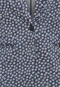 Gros plan sur un blazer bleu marine avec un petit motif floral blanc et violet clair, un bouton noir unique et un col à revers cranté.