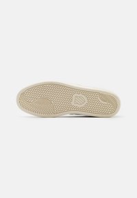 Sole of a sneaker featuring a textured rubber design with a herringbone pattern, colored light beige with a beige outsole edge.