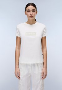 Hvid bomulds T-shirt med korte ærmer, der har et rektangulært logo i lys beige på forsiden. Enkel, afslappet pasform.