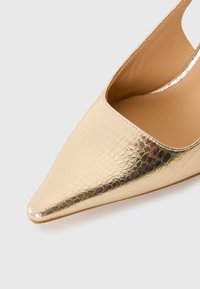Chaussure à talon haut texturée en or avec une pointe pointue et un design de talon ouvert. Doublure intérieure lisse, silhouette épurée et style minimaliste.