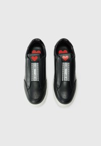 Zwarte leren instappers met perforatie in de neus, witte zool en rode hartenaccenten op de binnenzolen en hengsels met de tekst "OSCHINO LOVE MOSCHINO".