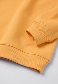 Geel sweatshirt met ribgebreide manchetten en zoom, zachte textuur en casual ontwerp. Stof lijkt glad met minimale stiksels.