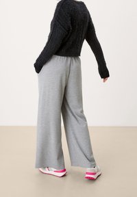 Šedé kalhoty s širokými nohavicemi a elastickým pasem, doplněné černým texturovaným svetrem a bílými teniskami s růžovými akcenty.