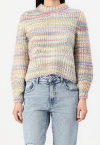 Wielokolorowy, dziergany sweter z wysokim kołnierzem, ozdobiony fakturowanym wzorem i długimi rękawami, zestawiony z wysokim stanem jeansów.