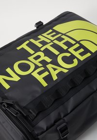 Sac à dos noir avec un grand texte jaune "THE NORTH FACE". Le matériau semble durable avec une finition texturée, des accents de fermeture éclair et de sangle visibles.