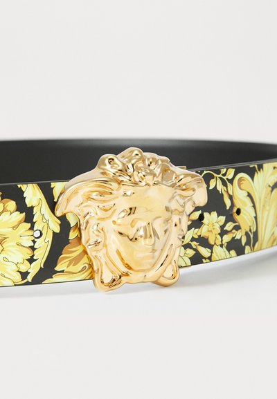 Schwarzer Gürtel mit einer auffälligen goldenen Medusen-Kopf-Schnalle und einem floralen gelben Muster entlang des Riemens, aus einem glatten, lederähnlichen Material gefertigt.