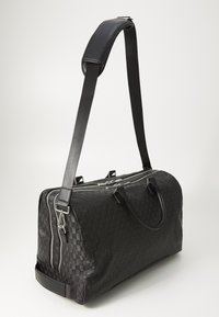 Bolsa de viaje negra con patrón tejido, asas de cuero y correa de hombro desmontable. Cuenta con cremalleras plateadas y detalles en metal.