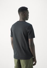 Camiseta de algodón negra con mangas cortas y cuello redondo, con una textura suave y un diseño sencillo, combinada con pantalones cortos de color verde oliva.