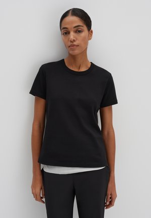 T-shirt in cotone nero con collo rotondo e maniche corte. Tessuto morbido, vestibilità rilassata, sovrapposta a una maglietta grigia chiara all'orlo.