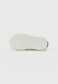 Sola de sapato branca com uma superfície texturada e padrão, salto arredondado e um discreto rótulo da marca na parte traseira. Design plano e flexível.
