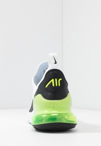 Nike Air Max 270 sneakers med en vit överdel, svarta detaljer, neongrön häl och synlig luftdämpning. Texturerat tyg och logodetaljer.