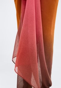 Διάφανο ύφασμα με βαθμιαία αλλαγή από ροζ σε καφέ, draped πάνω από παντελόνι καμένου πορτοκαλί, με φόντο λευκό.