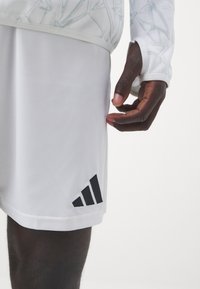 Hvide sports-shorts lavet af glat stof, med et sort Adidas-logo og tre skrå striber på den nederste venstre side.