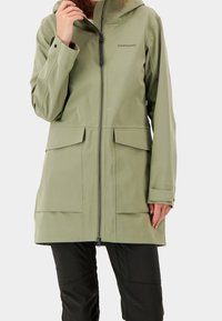 Ljusgrön vattentät jacka med huva, dragkedja och två stora framfickor. Har en slät yta och en modern design.