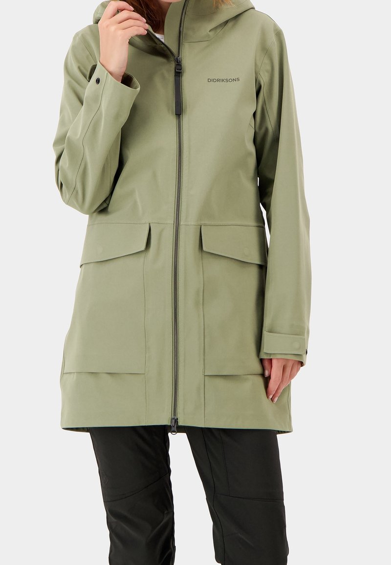 Ljusgrön vattentät jacka med huva, dragkedja och två stora framfickor. Har en slät yta och en modern design.