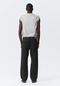 Sleeveless gray shirt with rolled edges, paired with black denim jeans featuring two back pockets and a loose fit.