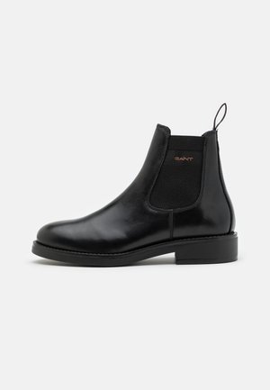 Black leather Chelsea boot with elastic side panel, pull tab, rounded toe, and flat sole. Sleek design with subtle stitching details.