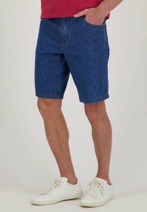 Shorts en jean bleu foncé à coupe droite, avec des passants de ceinture et une poche avant unique, portés avec des baskets blanches.