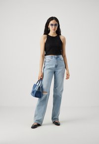 Fekete csipkés crop top, világoskék, magas derekú farmernadrág, amit szakadás díszít, kék kézitáska és napszemüveg. Lapos fekete cipők egészítik ki az összeállítást.