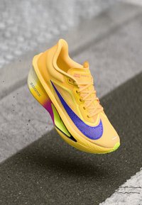 Nike Zoom Fly 06 skriešanas apavi spilgtā dzeltenā krāsā, ar purpura zīmolu, krāsainiem akcentiem, sietveida augšdaļu un vieglu, elegantu dizainu.