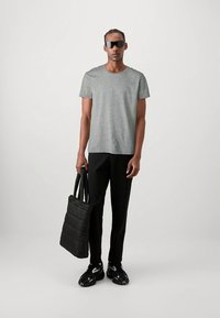 Szary T-shirt z krótkim rękawem, czarna pikowana torba na ramię, czarne zwężane spodnie i czarne sportowe buty, z ciemnymi okularami przeciwsłonecznymi. Prosty, nowoczesny styl.