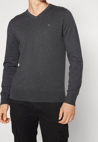 Dunkelgrauer V-Ausschnitt-Pullover aus weichem Strickstoff, mit langen Ärmeln und einem kleinen Logo-Detail auf der Brust.