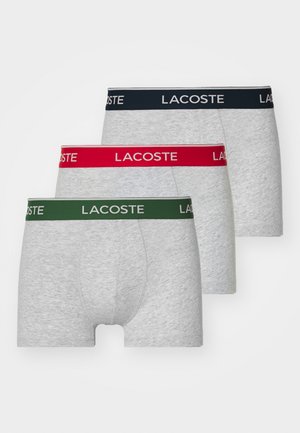 Three pairs of gray boxer shorts with elastic waistbands. Each has a different colored band: navy, red, and green, featuring the "LACOSTE" logo.