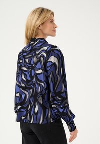 Langärmliges Oberteil mit fließendem Design in Blau und Schwarz, das abstrakte Muster und strukturierte Bündchen aufweist. Glattes Material mit lockerer Passform.
