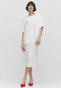 Löspassande vitt linne med korta ärmar, kombinerat med en knä-lång silverkjol med blommönster och röda spetsiga skor.