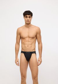 Czarny thong Calvin Klein z elastycznym paskiem z logo. Materiał wydaje się gładki i dopasowany, zaprojektowany dla minimalnego zakrycia i wygody.