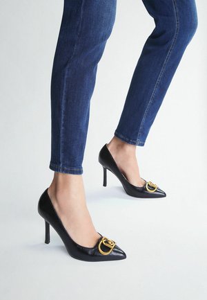 Décolleté neri in pelle con punta affusolata e tacca alta, accentuate da dettagli in oro nella parte anteriore. Indossate con jeans blu scuro a lunghezza caviglia.