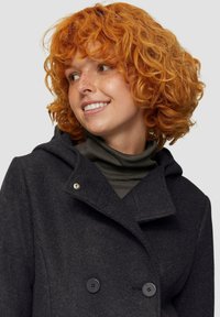 Dunkelgrauer Wollmantel mit doppelter Knopfleiste, großem Kapuze und silbernen Knopfakzenten, getragen über einem dunkelgrünen Rollkragenpullover.