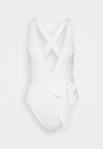 Vit baddräkt i ett stycke med djup V-ringning, korsade axelremmar och en sidoknytning. Slät textur med en åtsittande silhuett.