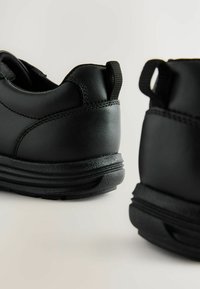 Schwarze Leder Schuhe mit glatter Textur, runder Form und dicker Sohle. Verfügt über eine Schlaufe an der Rückseite für ein einfaches Anziehen.