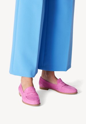 Lyserøde ruskinds loafers med flad hæl og en dekorativ frontrem, parret med blå vide bukser. Glat tekstur og klassisk design.