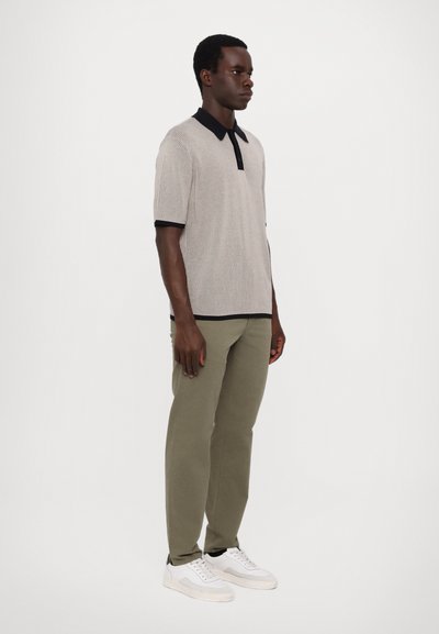 Polo shirt à rayures gris clair avec un col noir, associé à un pantalon vert olive et des baskets blanches. L'ensemble a un look décontracté et élégant.