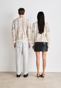 Pulover tricotat în bej cu modele albastre și albe; pantaloni gri lejeri; fustă mini din piele neagră, asortată cu sandale cu toc strălucitoare.