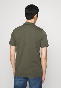 Olivově zelená polo tričko s krátkým rukávem a límečkem, vyrobené z měkké tkaniny, s zakřiveným sedlem na zadní straně a ohrnutými rukávy.