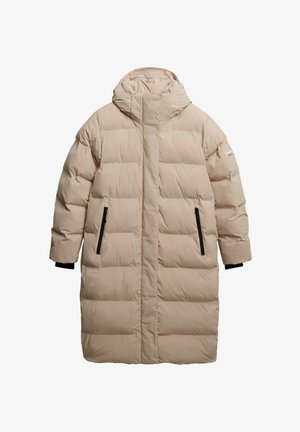 Manteau long matelassé en beige clair avec un col haut et une capuche, présentant des poches latérales zippées noires et des poignets côtelés. Texture lisse.