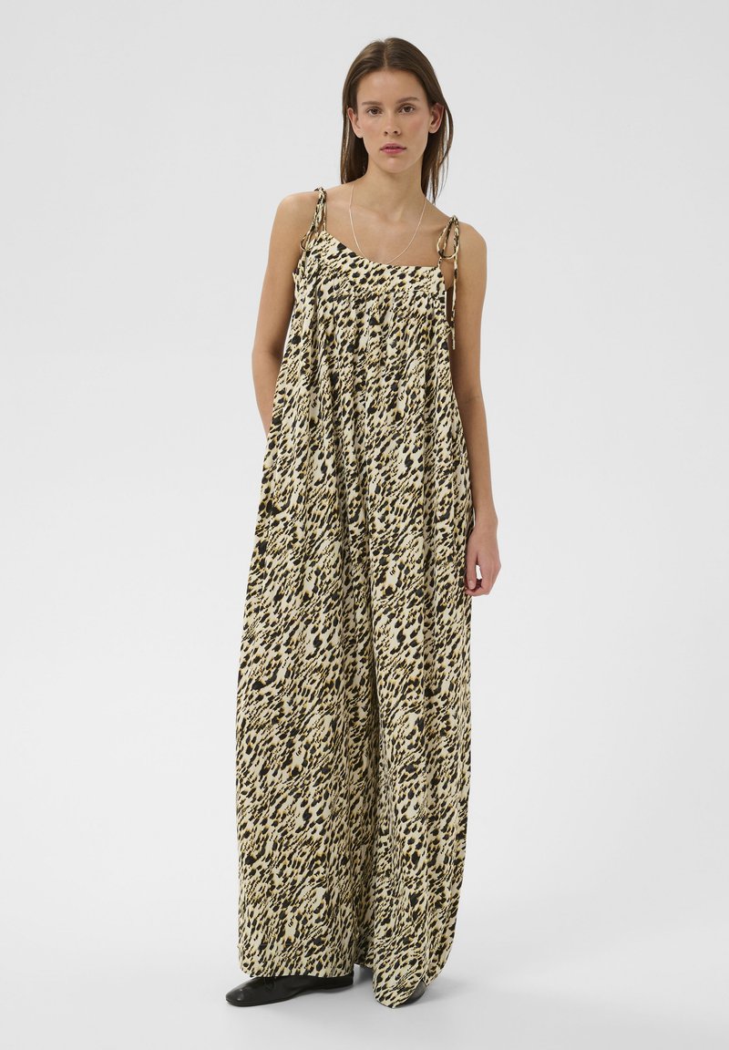 Robe longue en tissu léger, présentant un imprimé léopard noir et beige, des fines bretelles spaghetti, et une coupe ample et fluide avec des détails froncés.