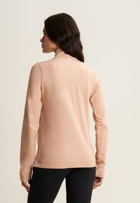 Top de manga larga rosa claro con cuello alto, de tela suave y diseño ceñido, combinado con leggings negros. Estilo minimalista.