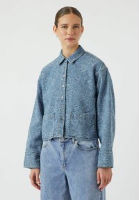 Giubbotto di denim tagliato di colore azzurro chiaro con motivo floreale in rilievo, chiusura con bottoni e due tasche frontali. Abbinato a jeans azzurro chiaro.