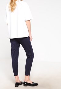 White short-sleeve top paired with navy slim-fit pants, featuring side slits at the ankle, completed with black patent loafers.